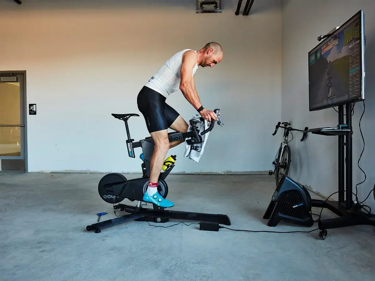 Man on a smart trainer, simulating spin classes with a virtual cycling game on a large screen.