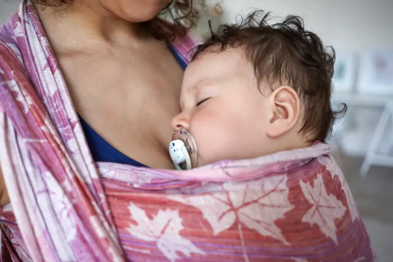Bambino addormentato con ciuccio, avvolto in una fascia colorata. Un momento di pace che segue l'orario allattamento.