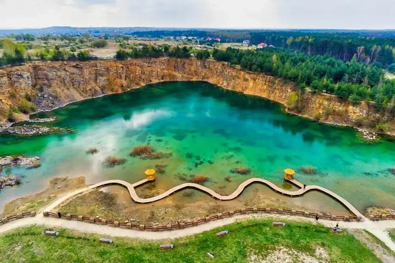 Malowniczy park Gr&oacute;dek z turkusową wodą w kamieniołomie, drewnianą kładką i otaczającym lasem.