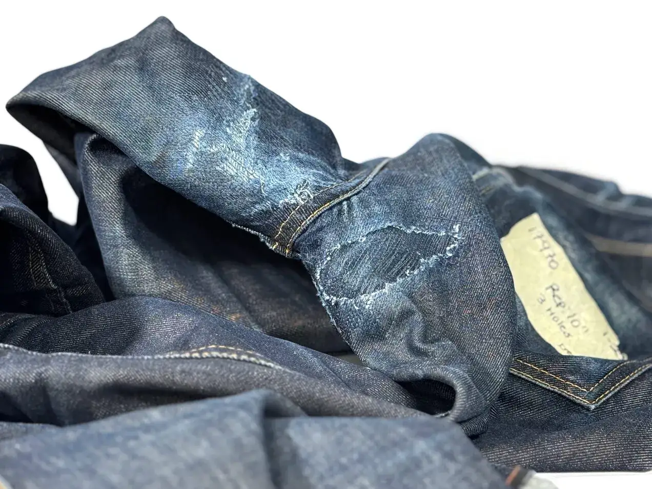 Close-up of dark denim jeans, showing visible stitching and wear, hinting at how to patch jeans.