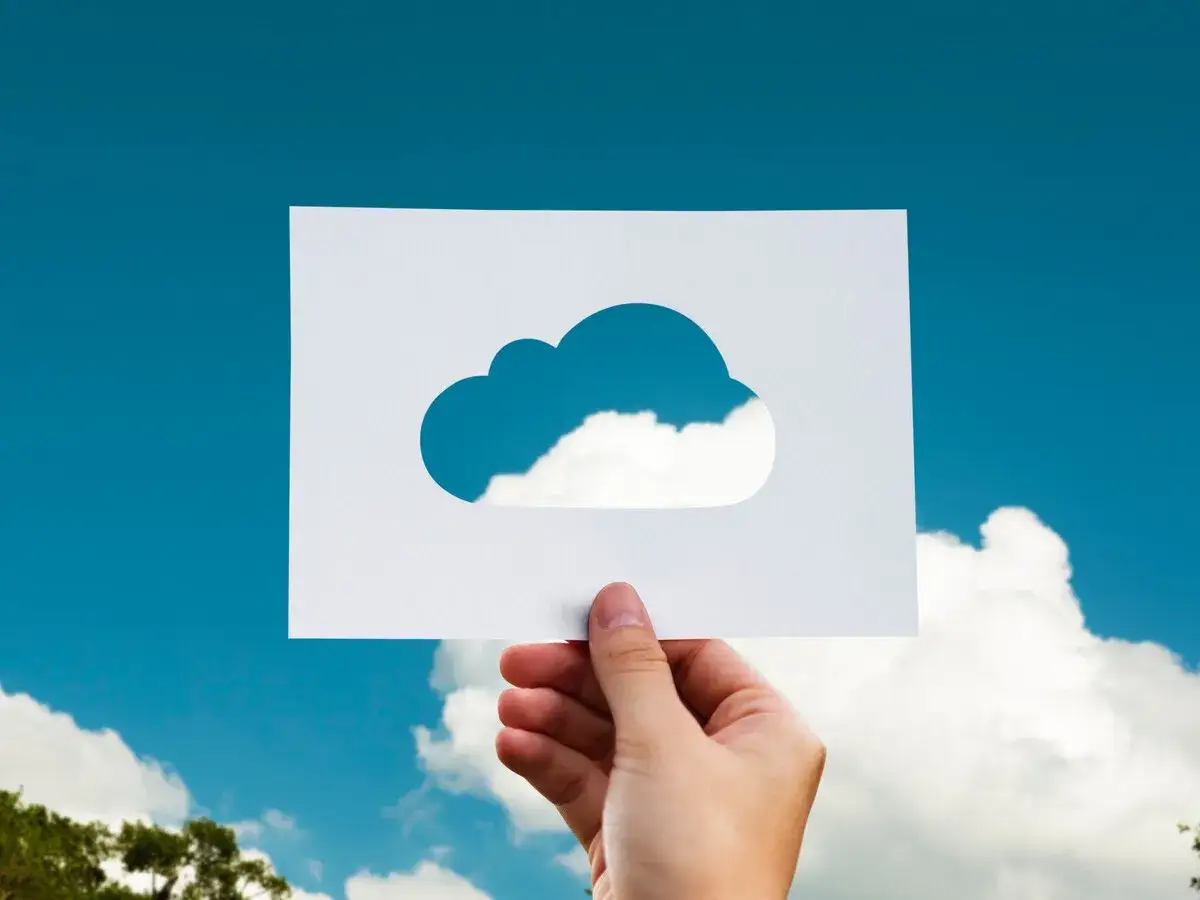 Mano sostiene papel con silueta de nube, mostrando el cielo real. Una met&aacute;fora visual de c&oacute;mo subir fotos a la nube.