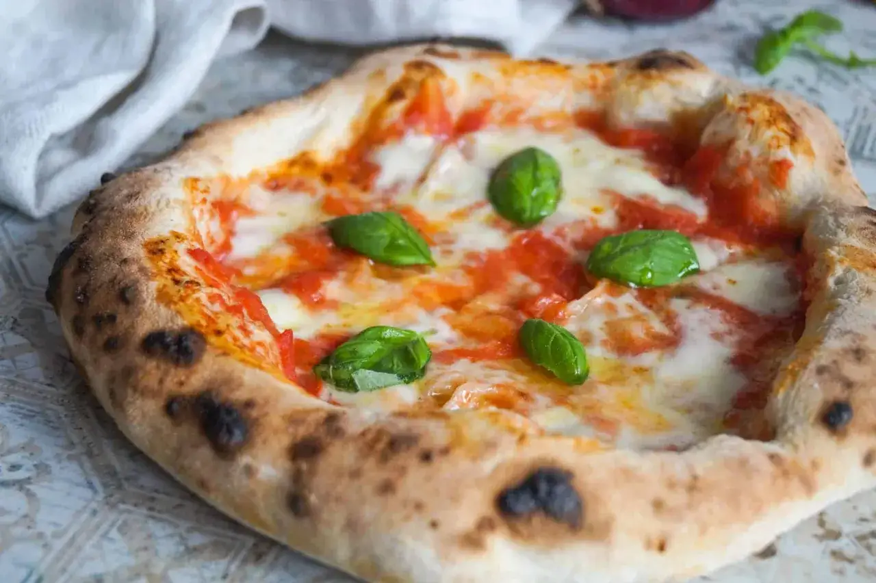 Pizza Margherita, un classico tra le migliori pizzerie Napoli, con pomodoro, mozzarella filante e basilico fresco.
