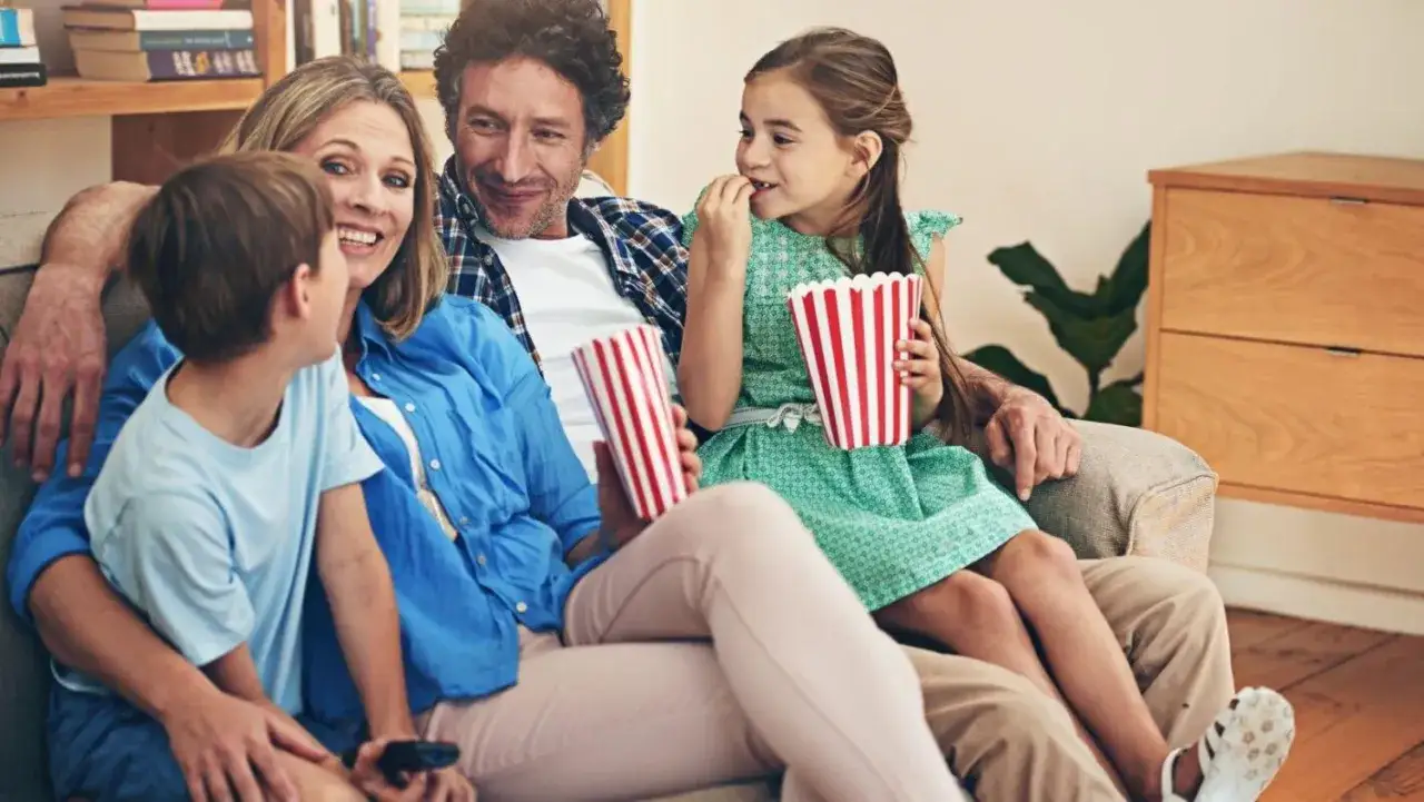 Rodzina ogląda filmy z przesłaniem, zajadając popcorn. Radość i wsp&oacute;lne chwile na kanapie.