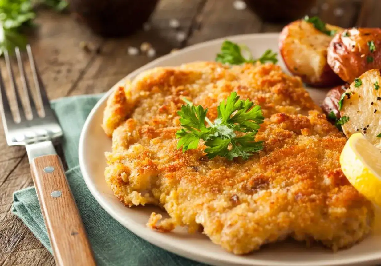 Złocisty kotlet po parysku, chrupiący i aromatyczny, podany z pieczonymi ziemniaczkami i cytryną. Pyszny obiad gotowy!