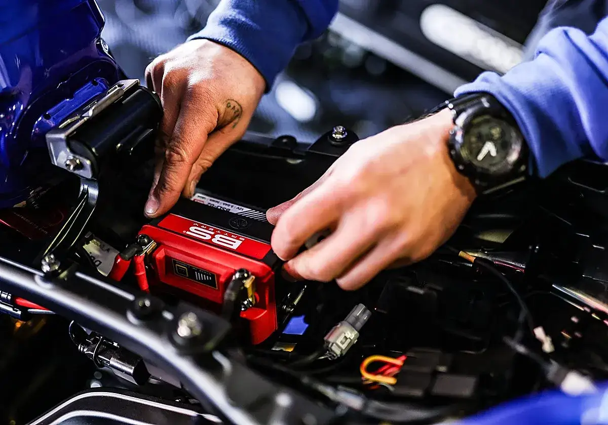 Man installing a red BS Battery. Saber cuanto dura una bateria de moto es clave para el mantenimiento.
