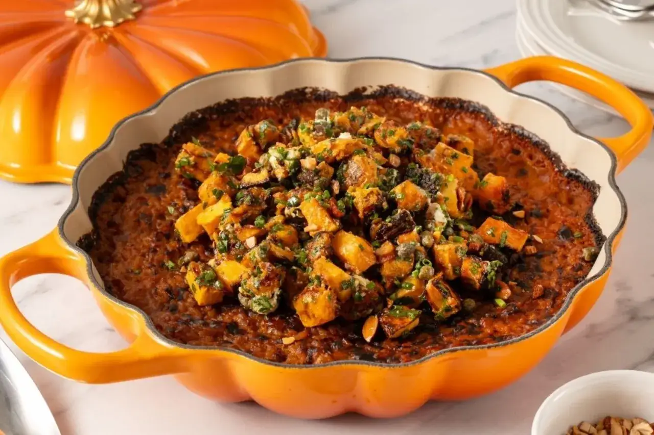 Un cremoso risotto de calabaza, cubierto con trozos de calabaza asada, hierbas frescas y frutos secos, servido en una cazuela naranja con forma de calabaza.