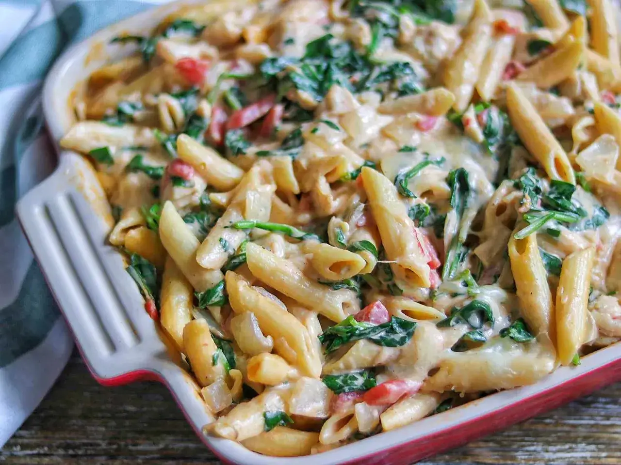 Penne w kremowym sosie ze szpinakiem i kurczakiem, zapiekane w naczyniu. Pyszne danie gotowe do podania.