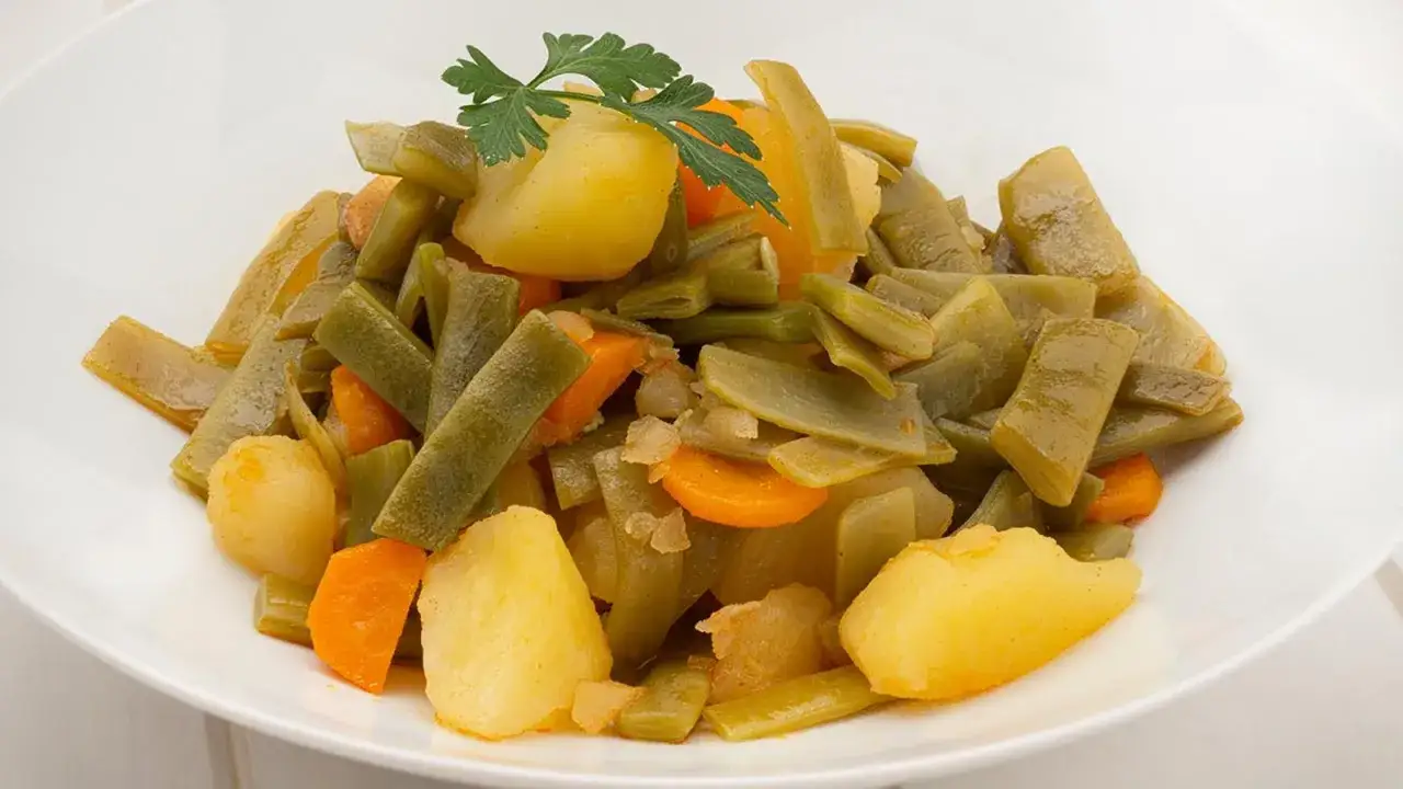 Un plato de judías verdes con patatas y zanahorias, decorado con perejil. Un guiso casero y saludable.