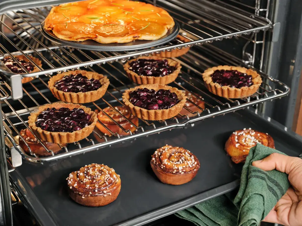 Varmluftsugn med flera pl&aring;tar samtidigt. En &auml;ppelkaka, bl&aring;b&auml;rstarteletter och kanelbullar bakas i ugnen.