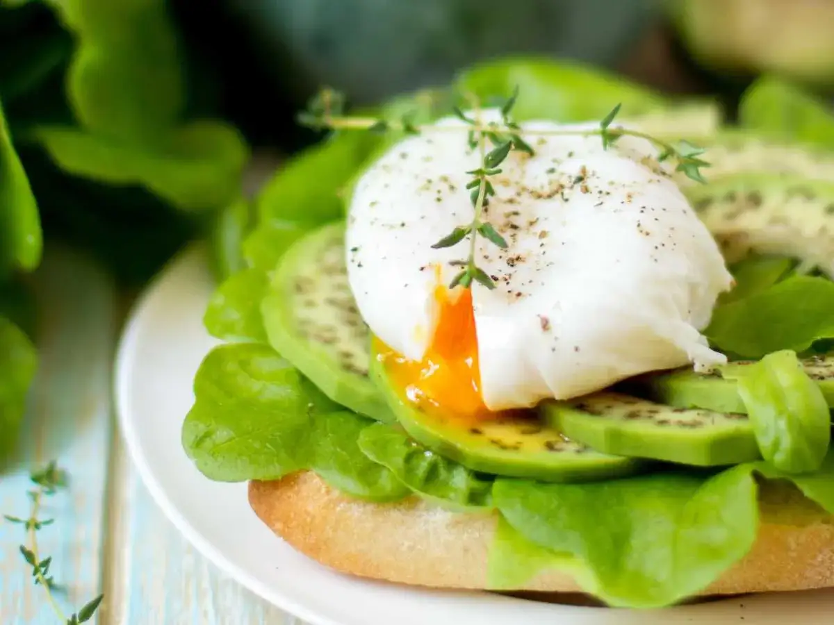 Tostada con aguacate, lechuga y un huevo pochado perfecto. Aprende como hacer huevos poche para un desayuno delicioso.