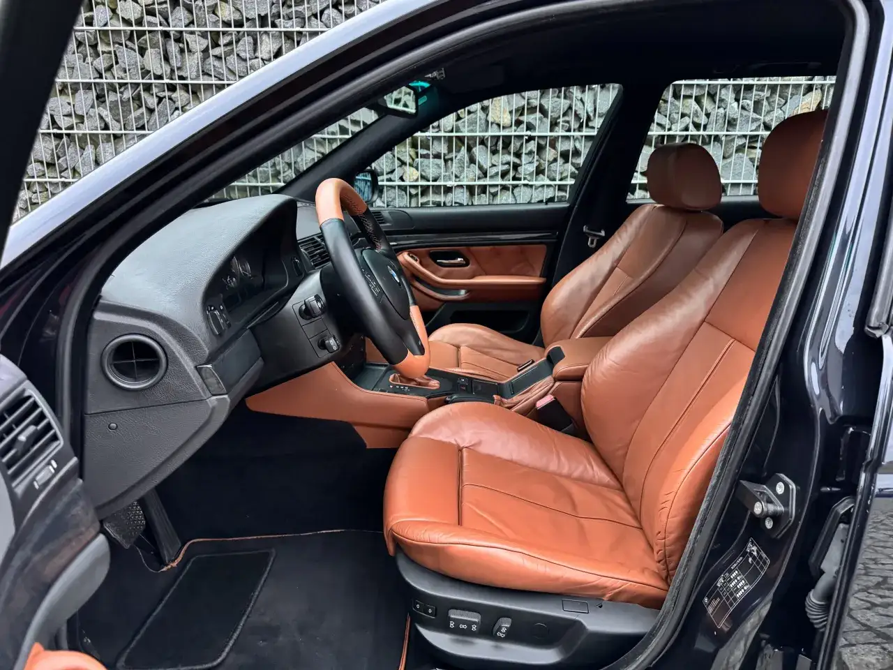 Wnętrze klasycznego BMW z brązową skórzaną tapicerką. Widok na fotele, deskę rozdzielczą i kierownicę. Te **bmw modele stare** zachwycają elegancją.