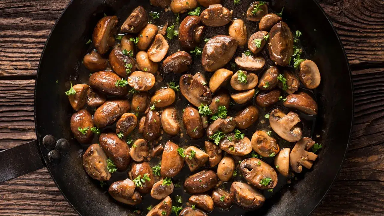 Gebratene Champignons in einer Pfanne, garniert mit Petersilie, duften verführerisch und warten darauf, genossen zu werden.