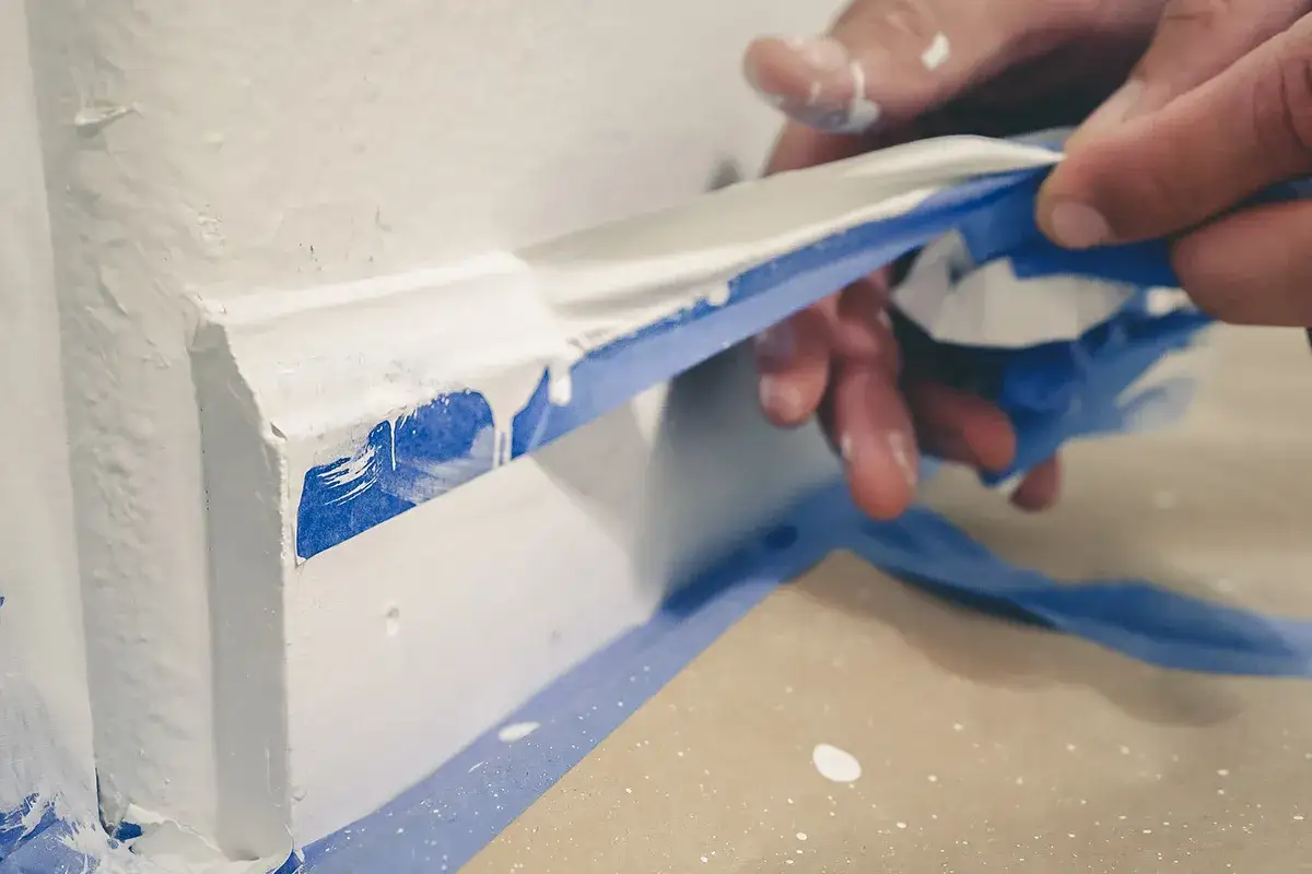 H&auml;nde ziehen blauen Malerkrepp ab, um Klebereste von Kunststoffrahmen zu entfernen.