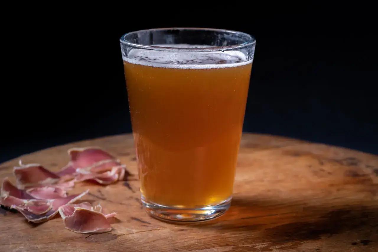Verre de bi&egrave;re norv&eacute;gienne ambr&eacute;e, mousse blanche, sur une table en bois avec des tranches de viande s&eacute;ch&eacute;e.