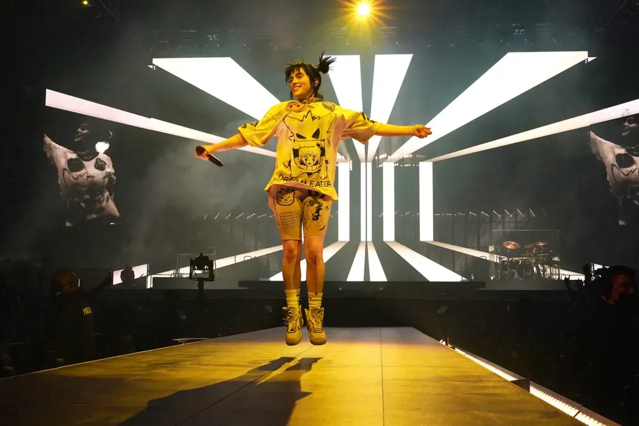 Billie Eilish skacze na scenie, trzymając mikrofon, szczęśliwsza niż kiedykolwiek.