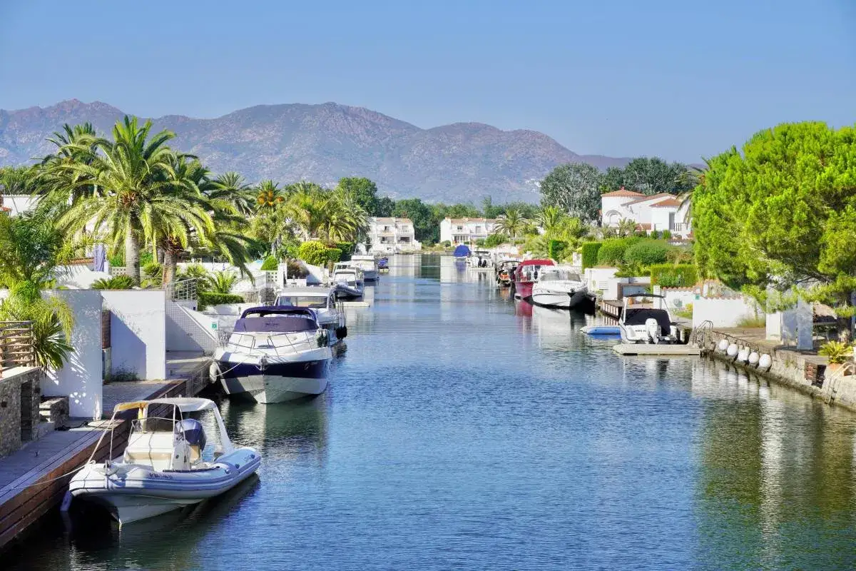 Canal pittoresque à Empuriabrava, Espagne, bordé de maisons blanches, de palmiers et de bateaux amarrés.
