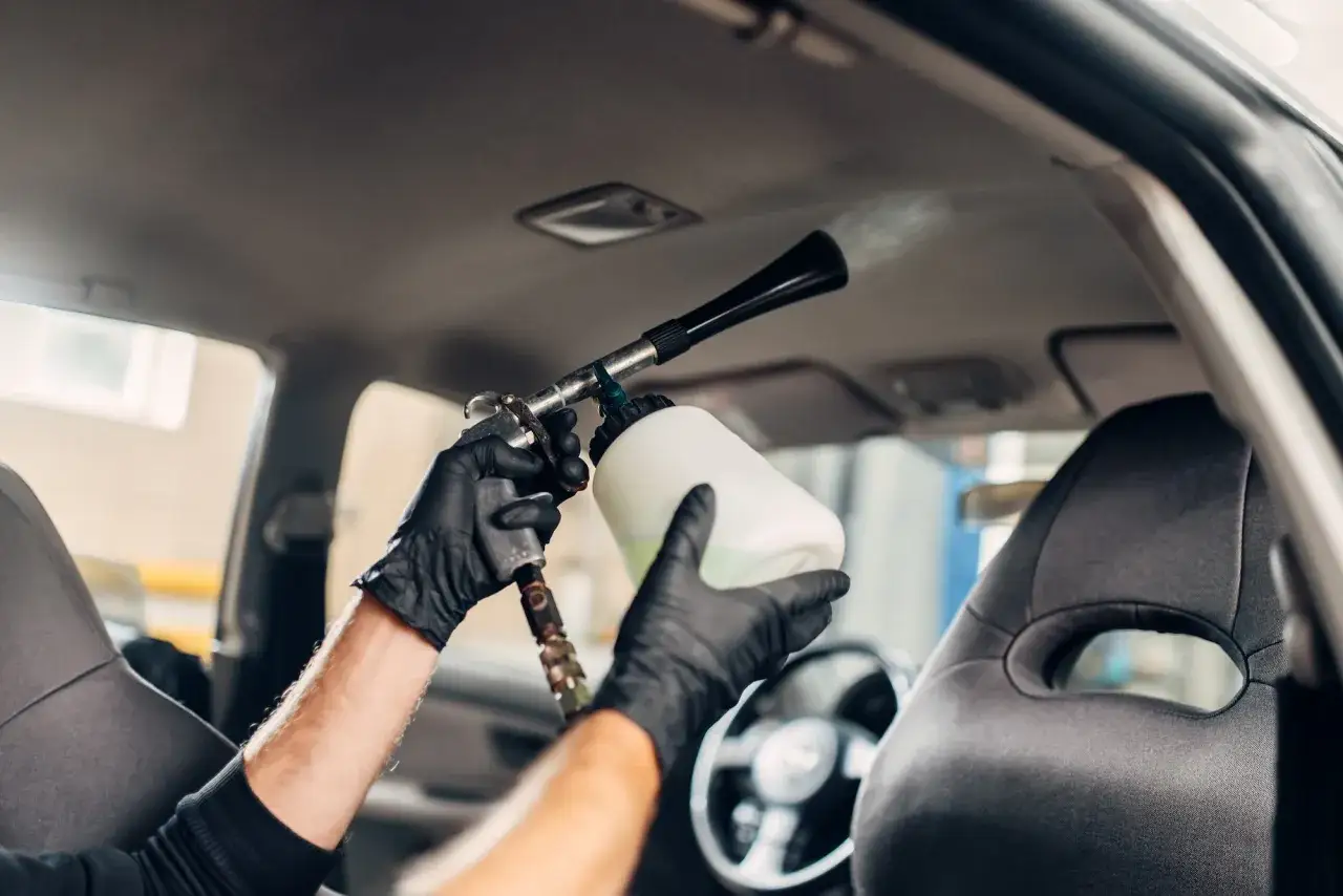 Man con guantes negros usa una pistola para limpiar el techo del coche, dejando el interior impecable.