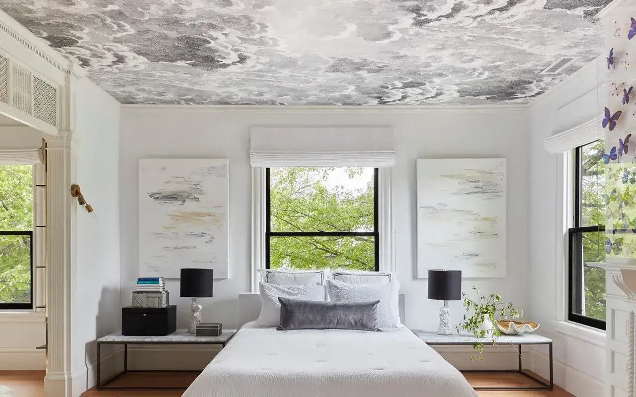Chambre avec un papier peint intissé c'est quoi, représentant un ciel nuageux sur le plafond. Le lit est blanc, flanqué de tableaux abstraits.