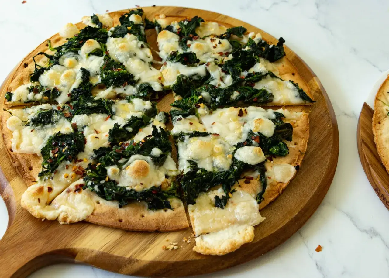 Pyszna pizza ze szpinakiem i ciągnącym się serem, posypana płatkami chili, podana na drewnianej desce.