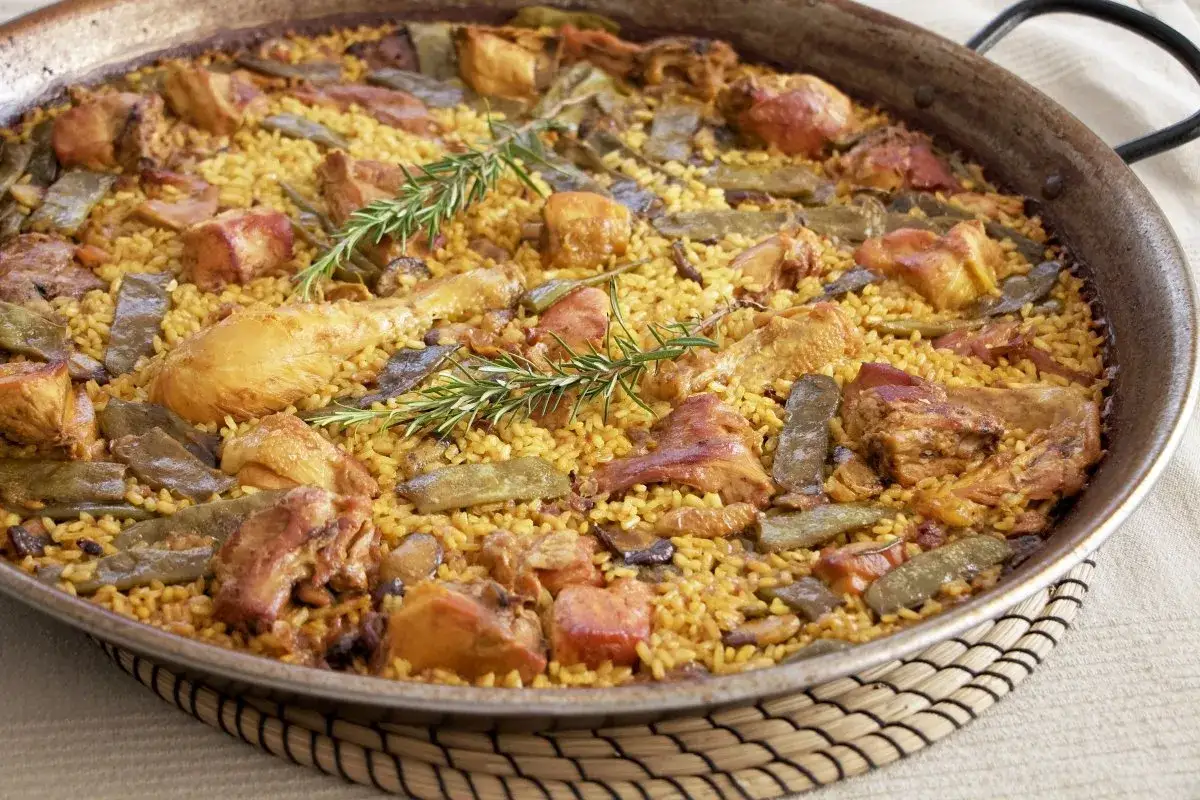 Paella de pollo y verduras, con arroz amarillo, trozos de pollo, judías verdes y romero. Los ingredientes paella lucen deliciosos.