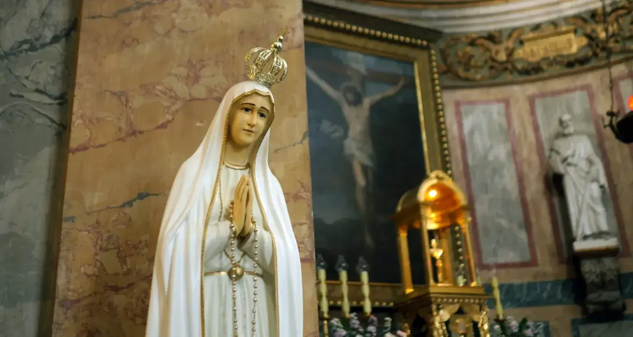 Figurka Matki Boskiej z Fatimy, z koroną na głowie, modląca się. W tle obraz Jezusa na krzyżu. Czy seks to grzech?