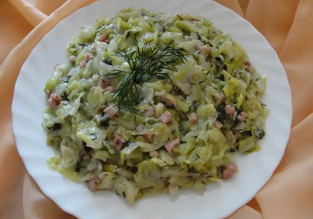 Młoda kapusta z kiełbasą, duszona z koperkiem, podana na białym talerzu.