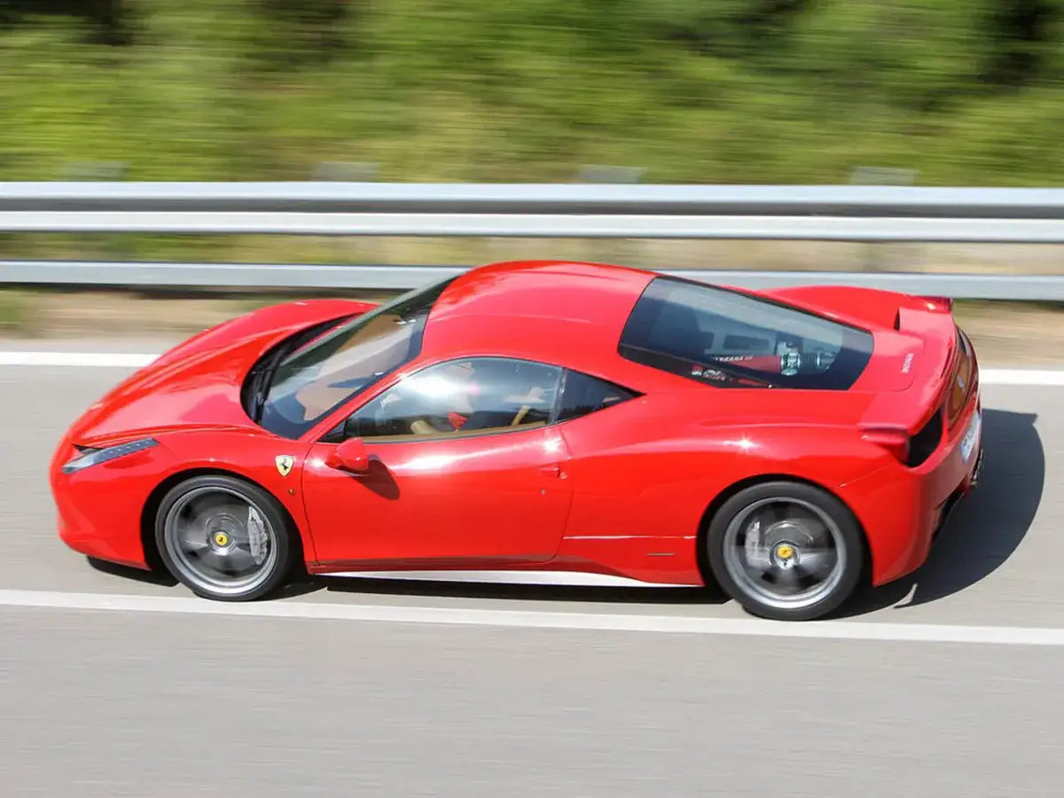 Czerwone Ferrari 458 pędzi po drodze, rozmazane tło sugeruje dużą prędkość.