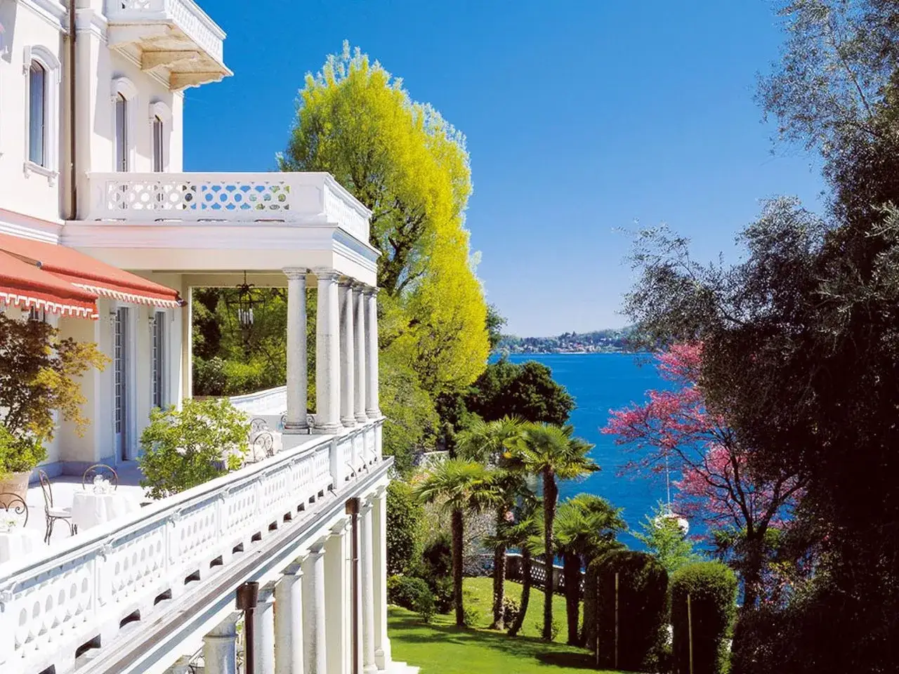Magnifique **h&eacute;bergement lac majeur** avec balcon blanc, vue sur le lac bleu et v&eacute;g&eacute;tation luxuriante.
