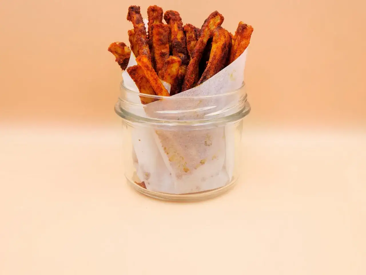 Chrupiące frytki z airfryer, przyprawione papryką, w szklanym słoiku wyłożonym papierem.