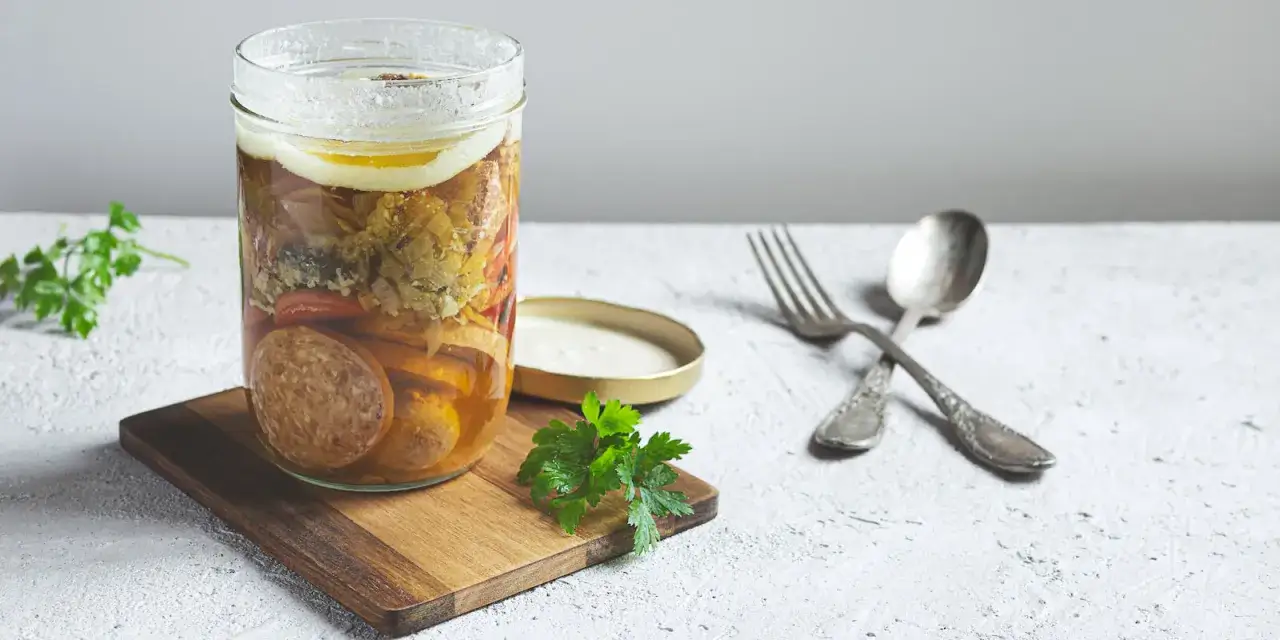 Ein Glas mit Fleisch und Gem&uuml;se, bereit zum Einkochen im Weckglas. Daneben liegen L&ouml;ffel und Gabel.