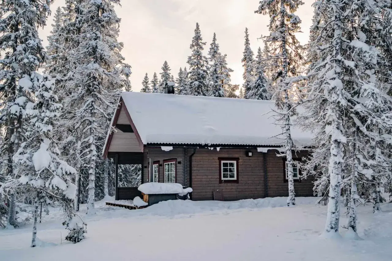 Mysig timmerstuga i Funäsdalens stugby, omgiven av snöklädda granar. En idyllisk vinterscen.