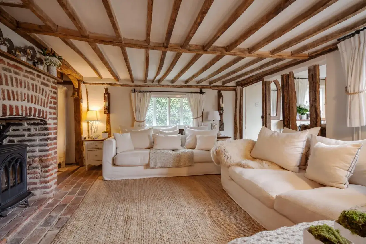 Salon chaleureux d'une maison style cottage anglais, avec poutres apparentes, chemin&eacute;e en briques et canap&eacute;s confortables.