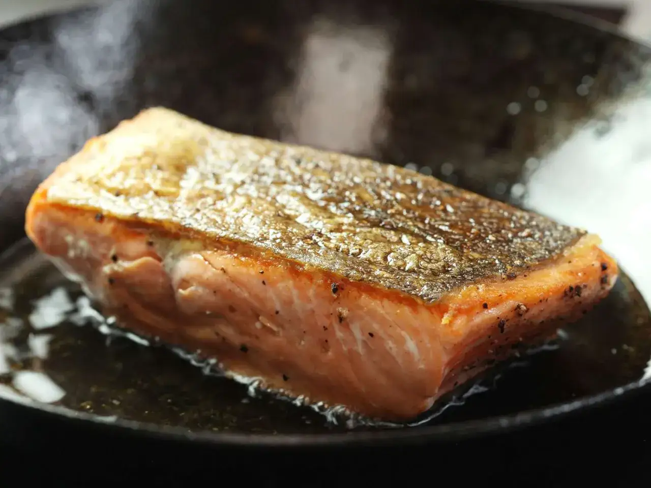 Ein saftiges St&uuml;ck Lachs braten in einer Pfanne, die Haut ist knusprig und goldbraun.