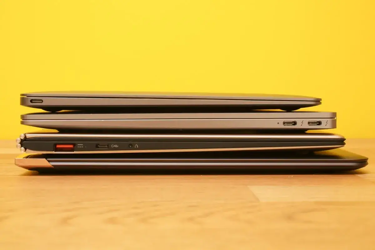 Stos pięciu laptopów, każdy z cienkim **bezel**em, na drewnianym blacie.