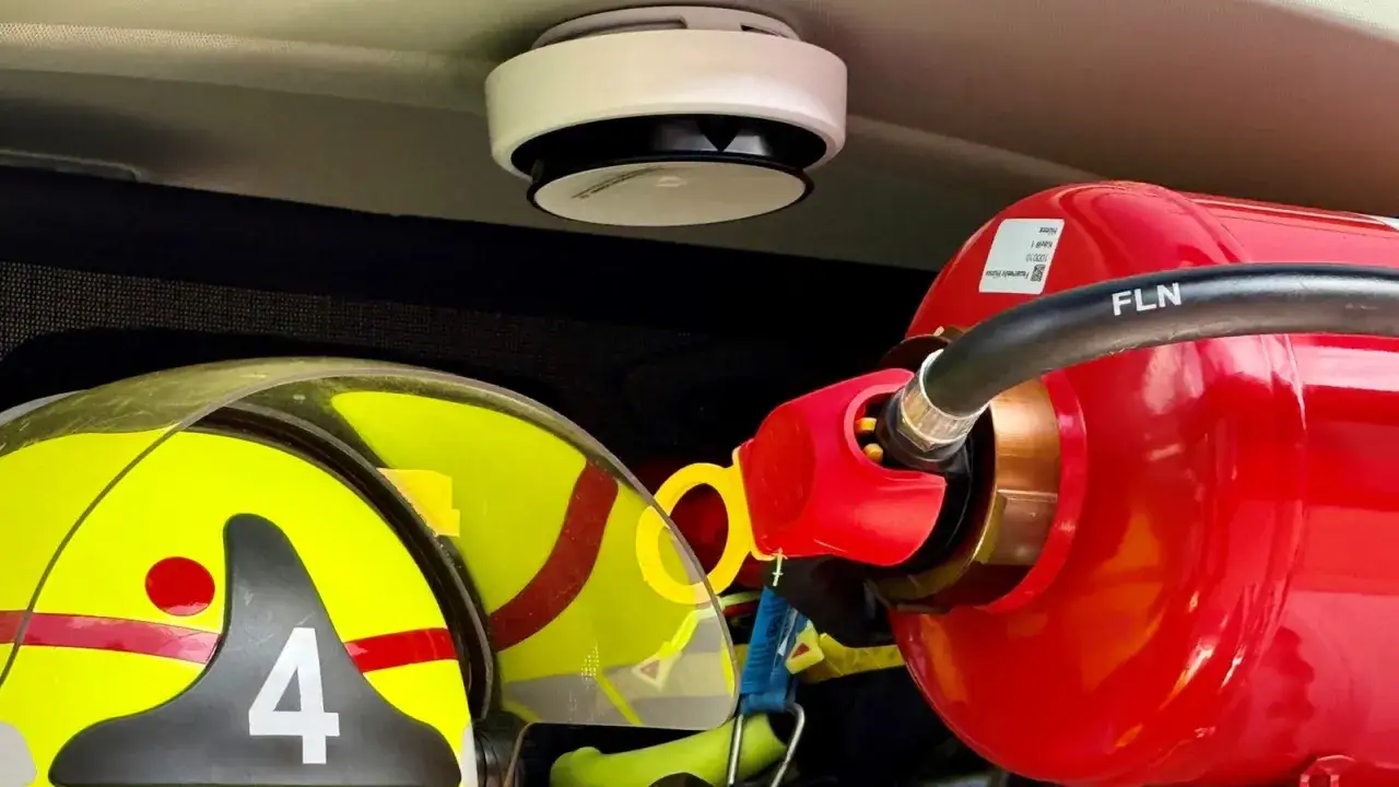 Ein Rauchmelder geht von alleine aus. Neben einem Feuerlöscher und einem Helm der Feuerwehr mit der Nummer 4.