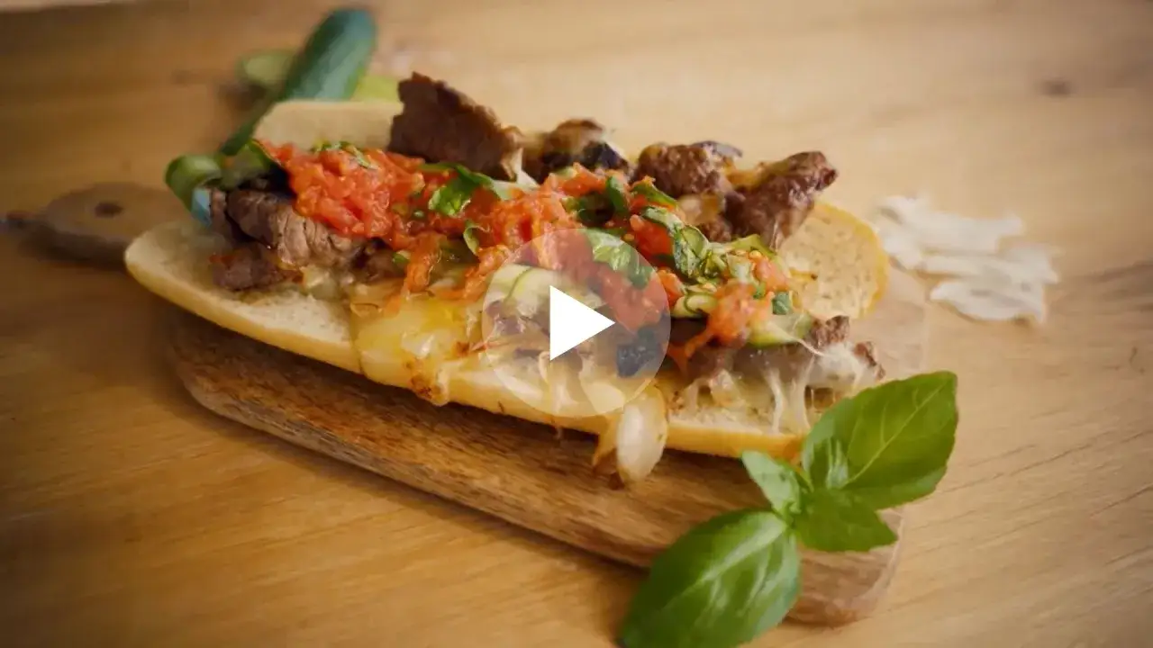 Pyszności na grilla: soczysty hot dog z grillowanym mięsem, serem, pomidorami i ziołami na drewnianej desce.
