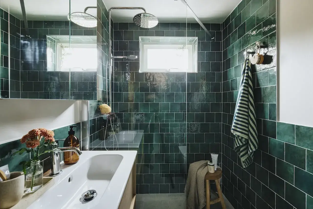 Ett modernt badrum med m&ouml;rkgr&ouml;na kakelplattor, en vit kommod med handfat och en duschh&ouml;rna. Perfekt f&ouml;r en renovering badrum.