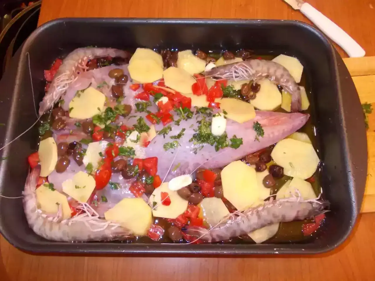 Coda di rospo al forno con patate, gamberi, olive e pomodorini, pronta per essere infornata.