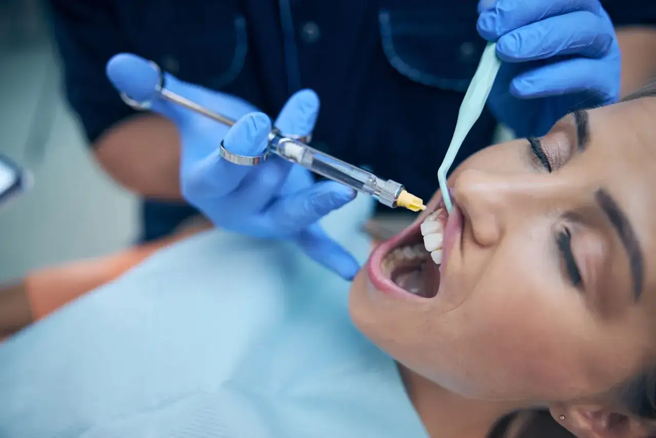 Il dentista esegue l'anestesia locale su una paziente. La siringa &egrave; tenuta da una mano guantata blu.
