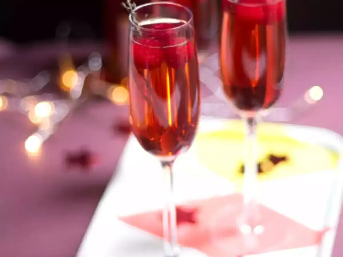 Deux flûtes de soupe de champagne, garnies de framboises, sur un plateau, avec des guirlandes lumineuses en arrière-plan.