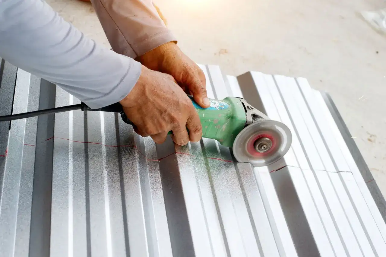 Ręce trzymają szlifierkę kątową, kt&oacute;ra tnie falistą blachę aluminiową wzdłuż czerwonej linii. To pokazuje, czym ciąć aluminium.