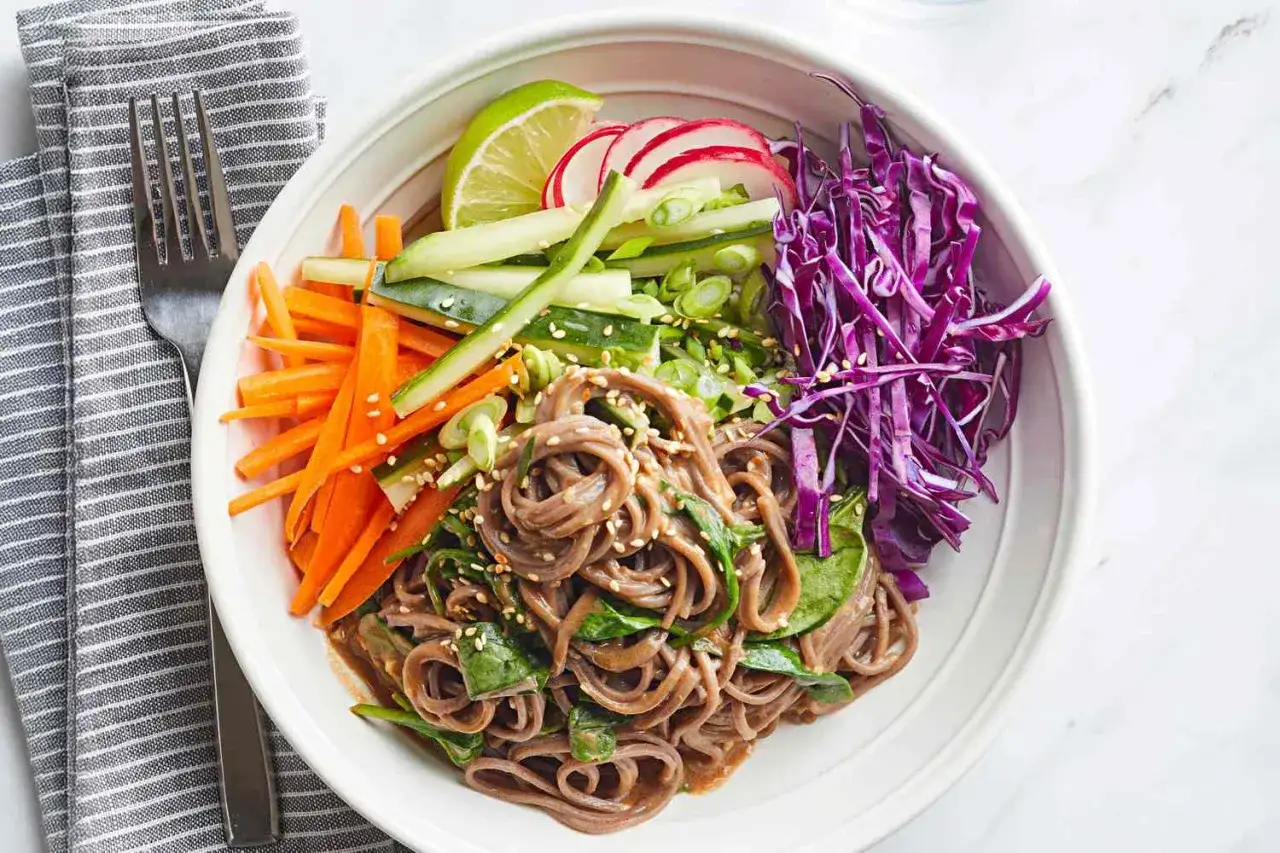 Kolorowa miska z makaronem soba, chrupiącymi warzywami: marchewką, ogórkiem, czerwoną kapustą, rzodkiewką i limonką. Idealny makaron soba przepis na lekki posiłek.