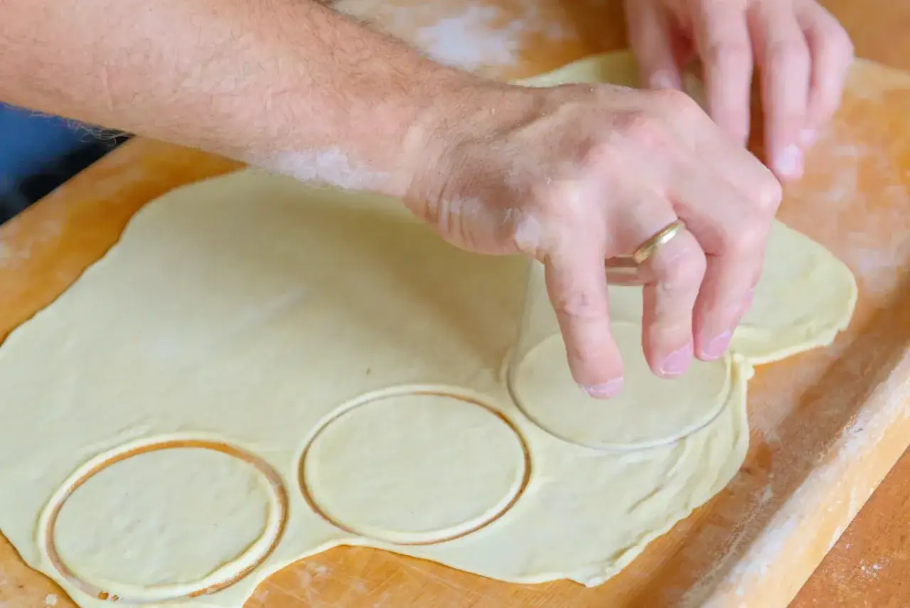 Ręce wycinają k&oacute;łka z ciasta na pierogi za pomocą szklanki.