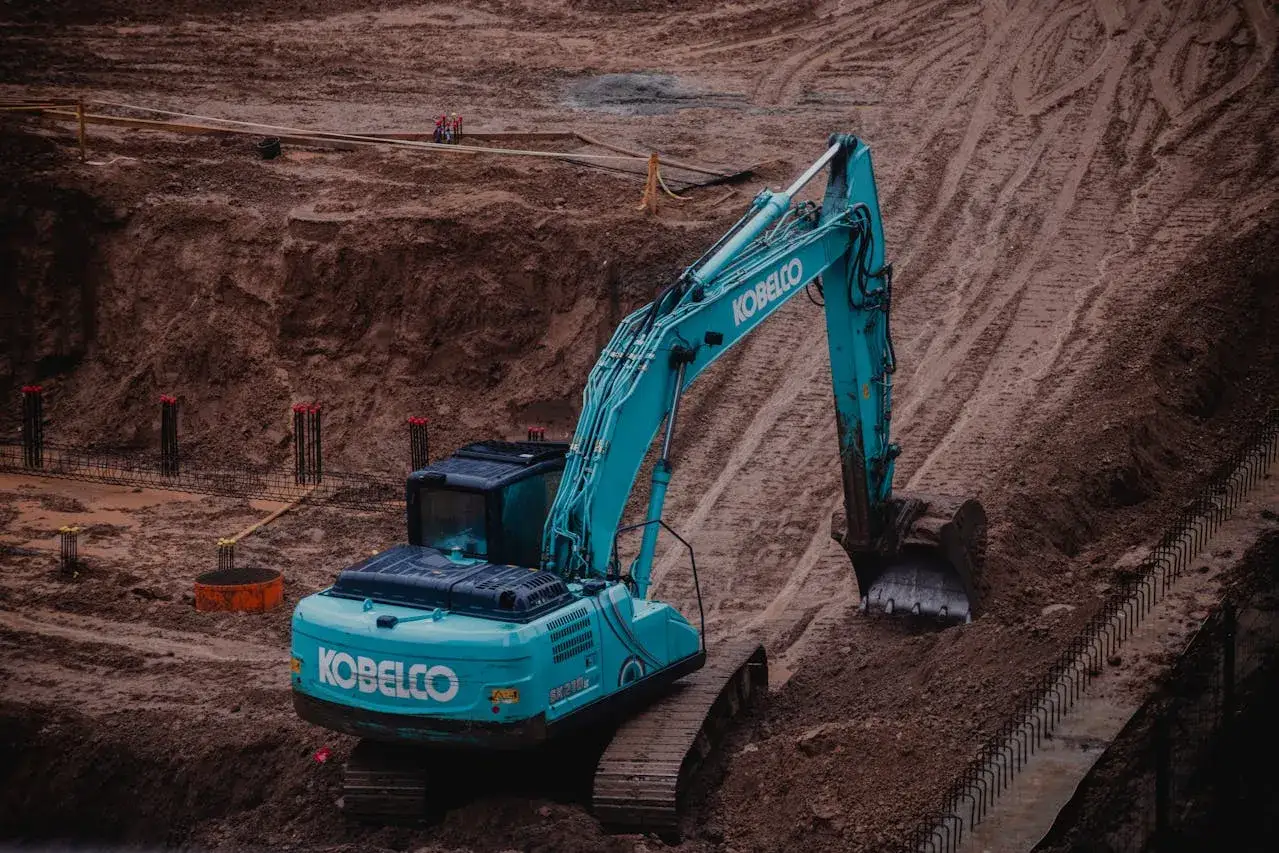 Turkusowa koparko-ładowarka Kobelco pracuje na budowie. Operatorzy tej maszyny mogą liczyć na dobre zarobki.