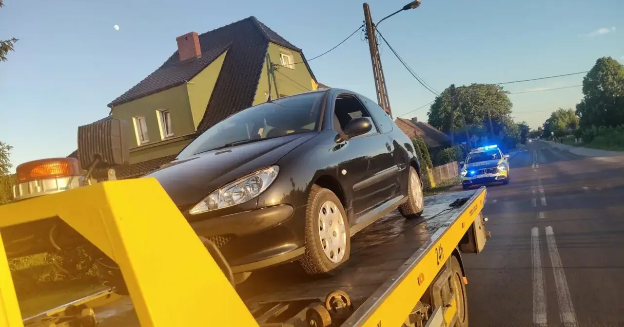 Czarny samochód na lawecie, obok radiowóz policyjny z włączonymi sygnałami świetlnymi. Zatrzymanie obywatelskie zakończone odholowaniem pojazdu.