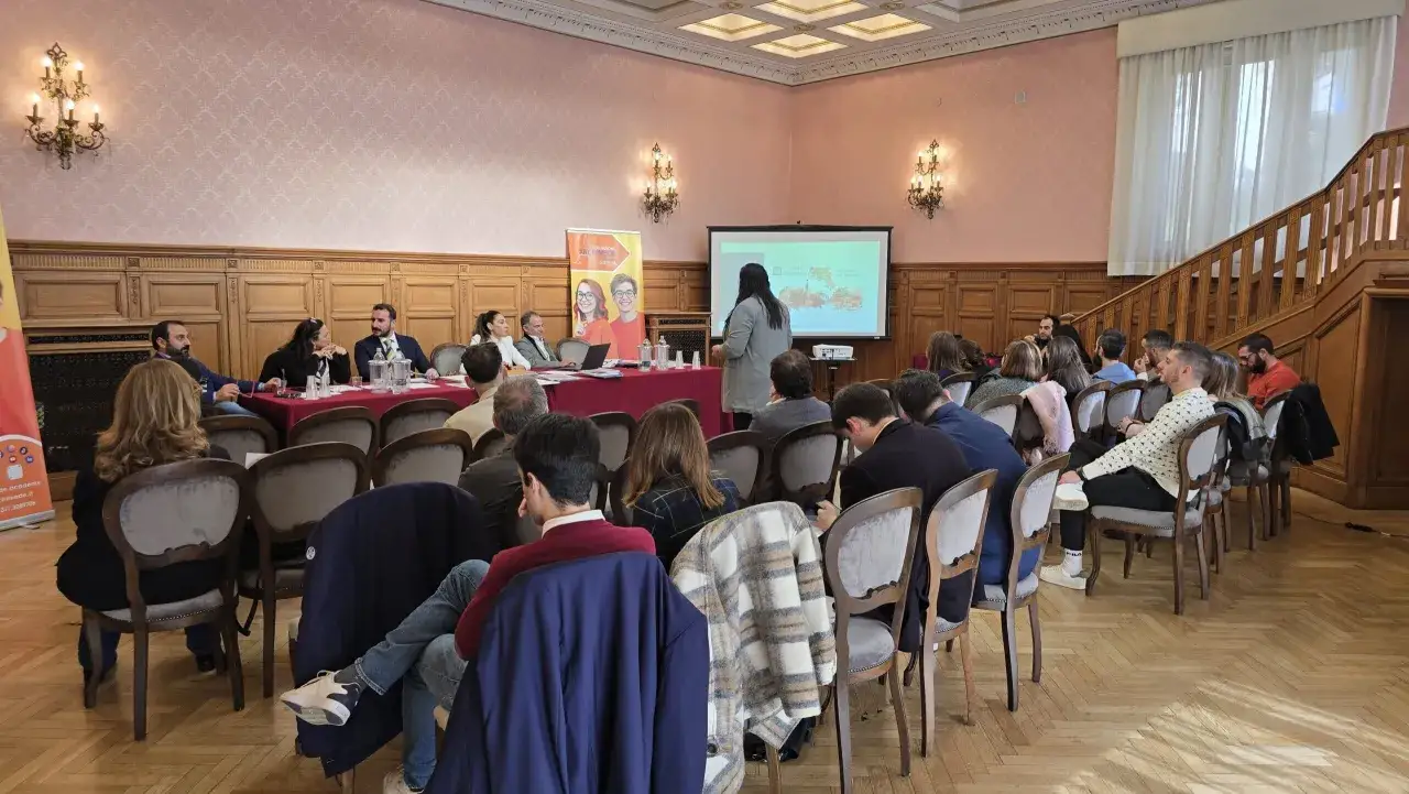 Presentazione alla Fondazione Archimede: relatori al tavolo e pubblico in sala, con un proiettore che mostra immagini.