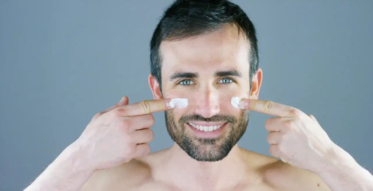 Cara hombre con crema hidratante en las mejillas, sonriendo.