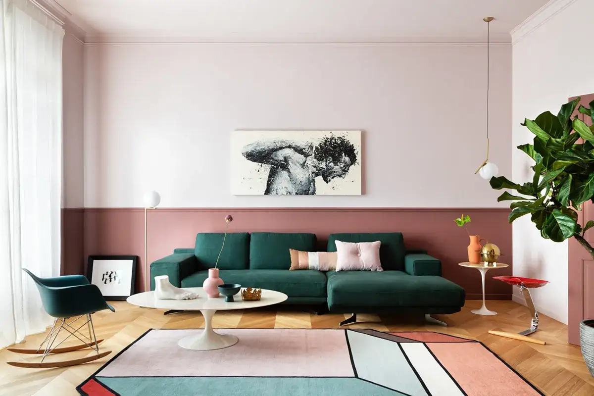 Soggiorno con pareti rosa antico e tortora, divano verde, tappeto geometrico e un quadro d'arte.