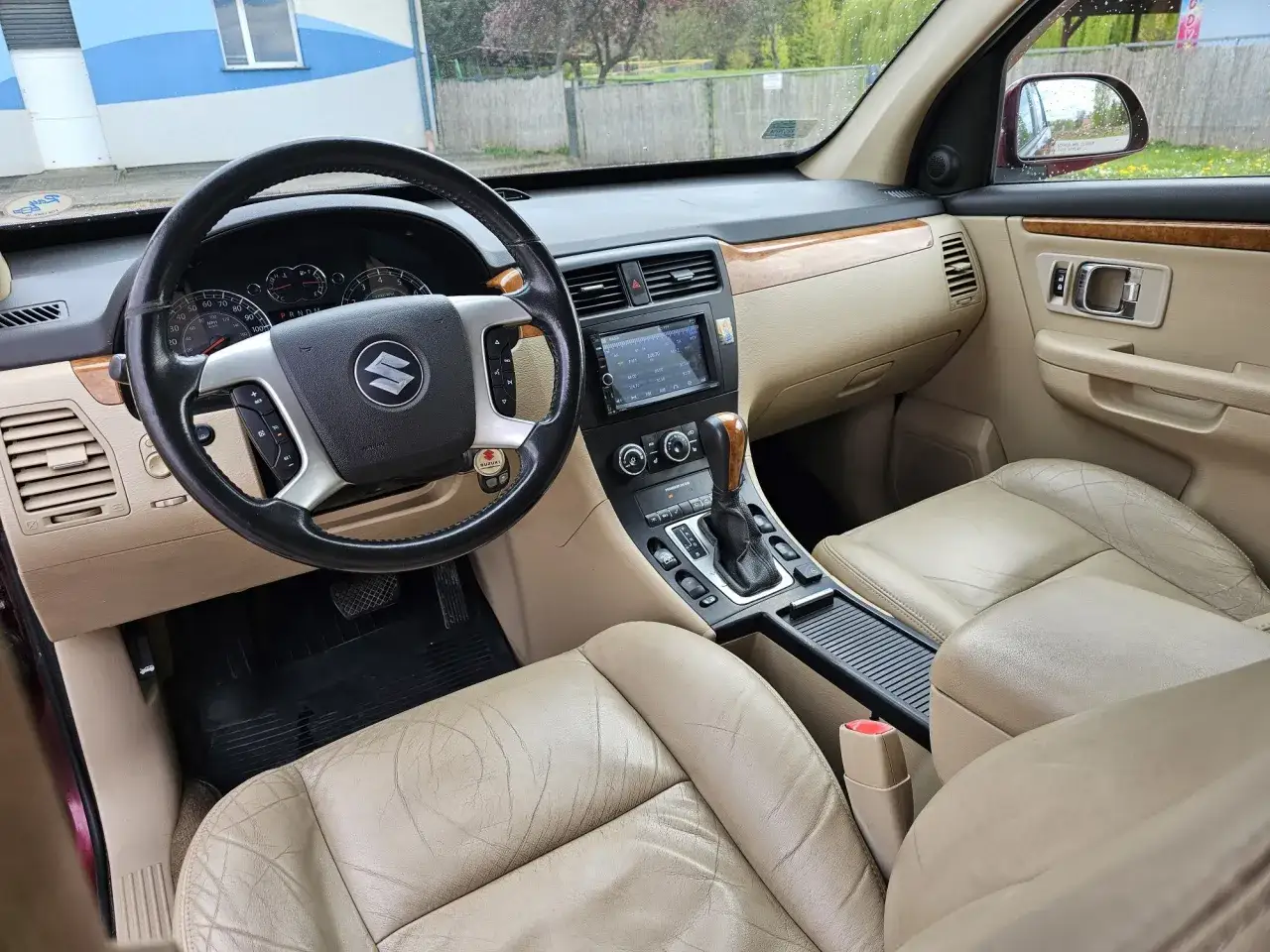 Wnętrze Suzuki XL7 z beżową skórzaną tapicerką, kierownicą i panelem środkowym.