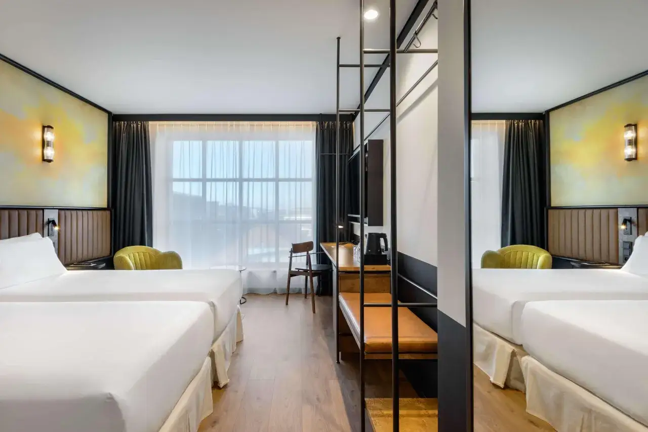 Pokój w Barcelo Hotel z dwoma łóżkami, żółtym fotelem i biurkiem.